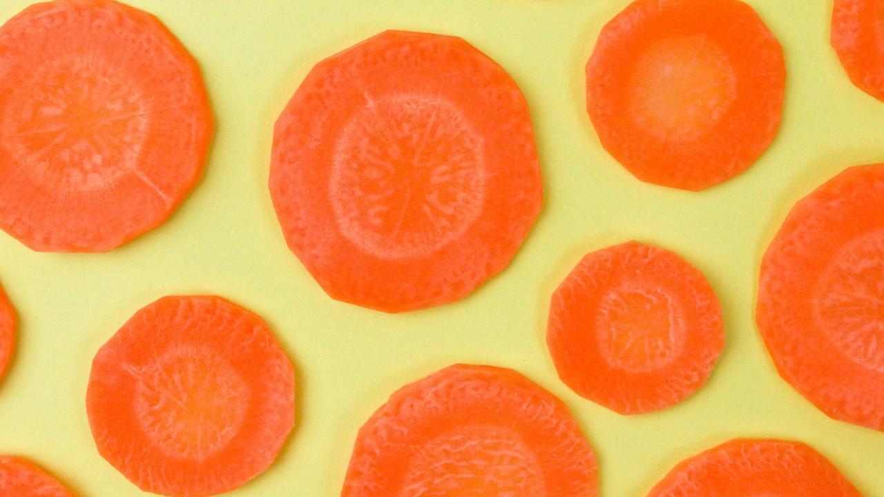 Mehrere Möhrenscheiben auf gelben Grund drapiert Mehrere Möhrenscheiben auf gelben Grund drapiert