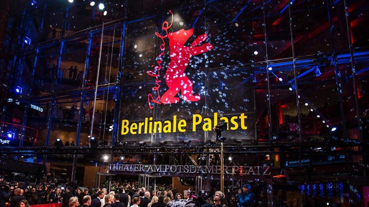 Der Berlinale-Palast am Abend, mit dem roten Bären an der Glasfront, davor viele Menschen auf und neben dem roten Teppich Der Berlinale-Palast am Abend, mit dem roten Bären an der Glasfront, davor viele Menschen auf und neben dem roten Teppich
