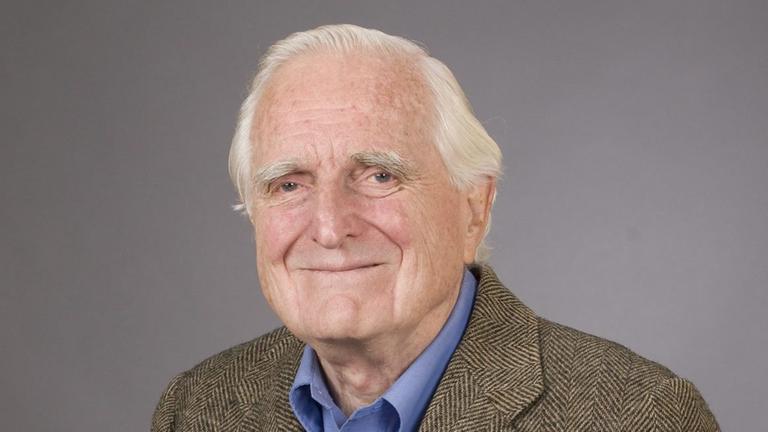 Ein Foto  des US-Computertechnikers Douglas Carl Engelbart, der  hält seine Erfindung: die erste Computer-Maus: in Kästchen, mit einem Kabel an einem Ende. Eoben einem roten Knopf zum Klicken und unten zwei Rädchen.