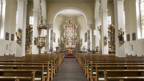 Innenaufnahme einer leeren Kirche mit Blick auf Bänke und Altar.