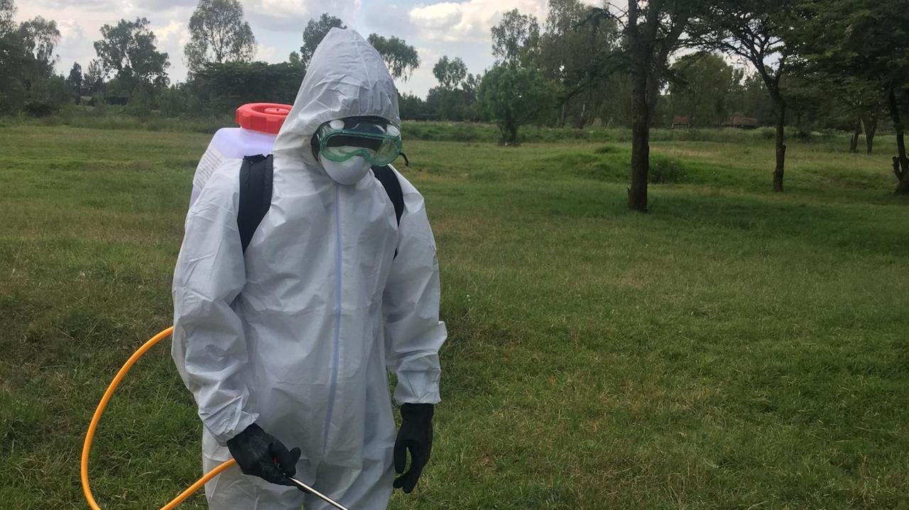 Ein Mann mit weißem Schutzanzug und Maske sprüht auf einer Wiese Pestizide gegen die Heuschreckenplage. 