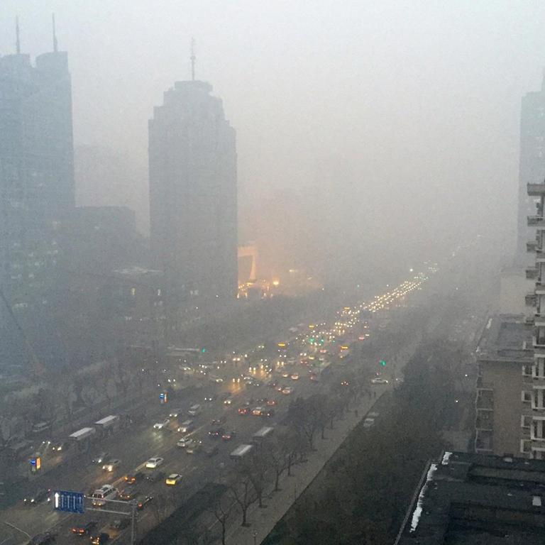 Eine graue Smogwolke hängt über den Wolkenkratzern und viel befahrenen Straßen Pekings