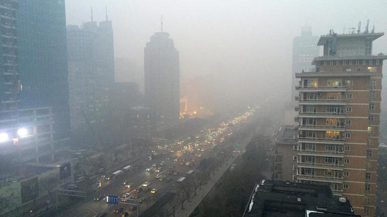 Eine graue Smogwolke hängt über den Wolkenkratzern und viel befahrenen Straßen Pekings