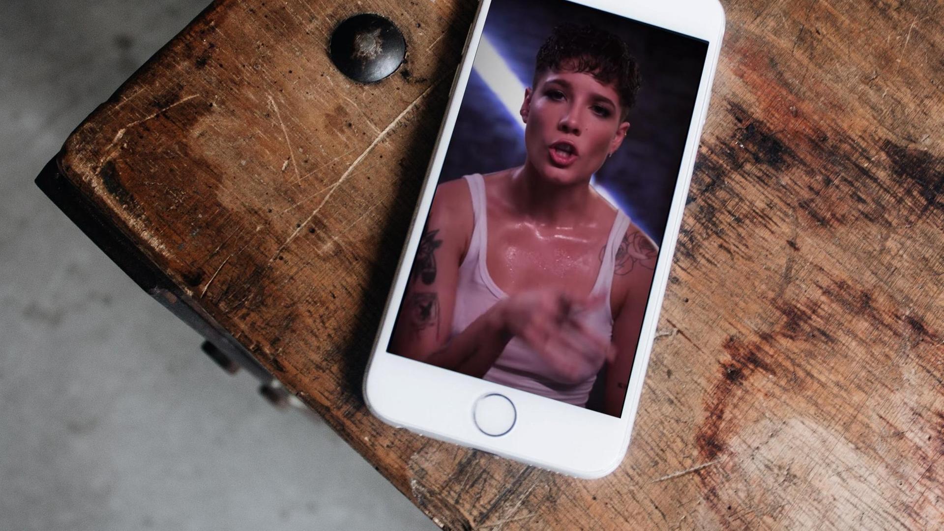 Auf einem Tisch liegt ein Smartphone auf dessem Display die Sängerin Halsey im Hochformat vollflächig zu sehen ist. Auf einem Tisch liegt ein Smartphone auf dessem Display die Sängerin Halsey im Hochformat vollflächig zu sehen ist.