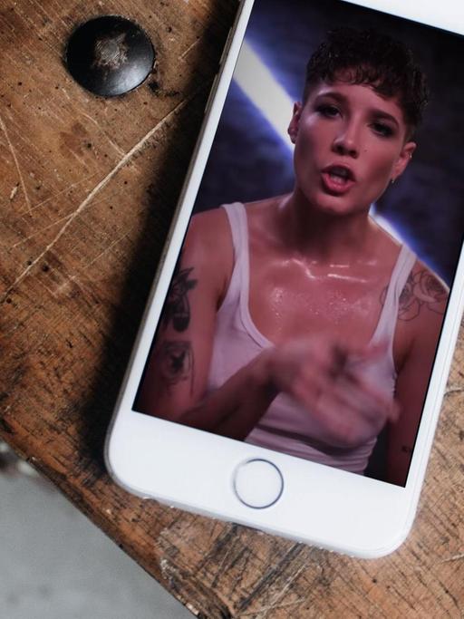 Auf einem Tisch liegt ein Smartphone auf dessem Display die Sängerin Halsey im Hochformat vollflächig zu sehen ist.
