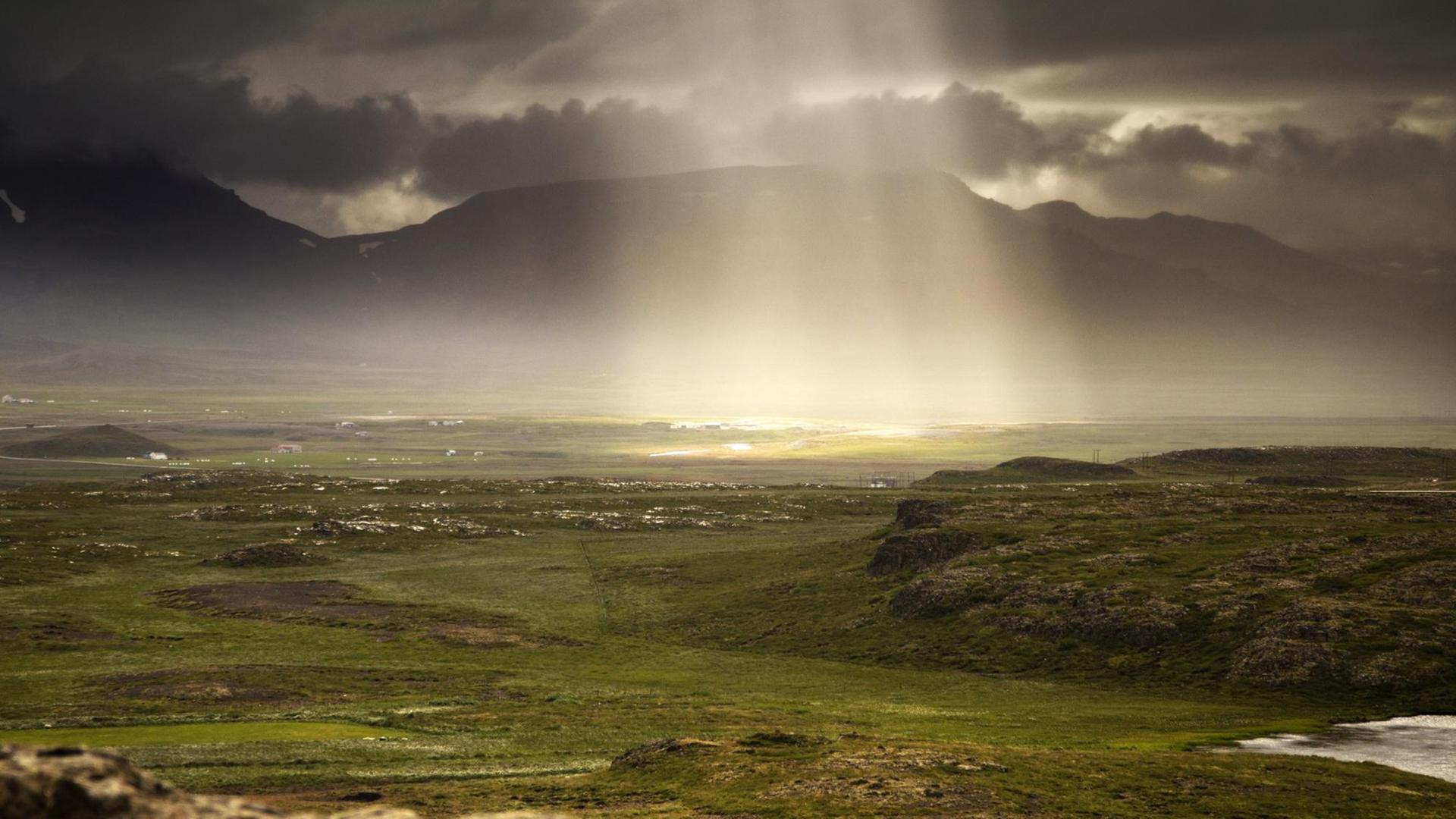 Sonnenlicht fällt durch die dichte, graue Wolkendecke auf die Landschaft Islands. Sonnenlicht fällt durch die dichte, graue Wolkendecke auf die Landschaft Islands.
