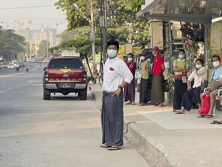 Einige Menschen stehen an einer Bushaltestelle in Rangun