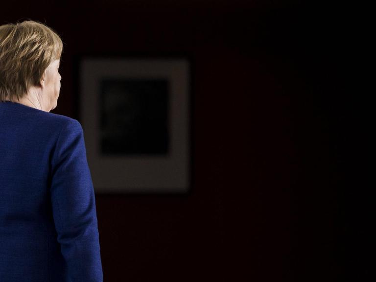 Bundeskanzlerin Angela Merkel, CDU, steht im blauen Blazer mit dem Rücken zur Kamera.