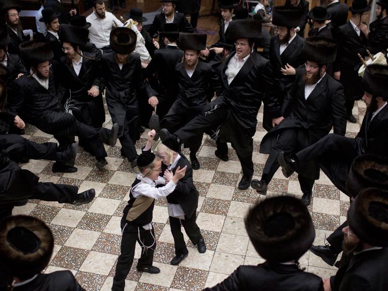 Jüdische Männer tanzen in einem Kreis, in der Mitte stehen zwei kleine Jungen.