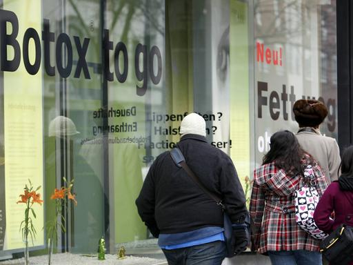 Passanten vor dem Schaufenster einer Schönheitspraxis in Berlin, die Botox-to-go und Fett-weg-Behandlung anbietet