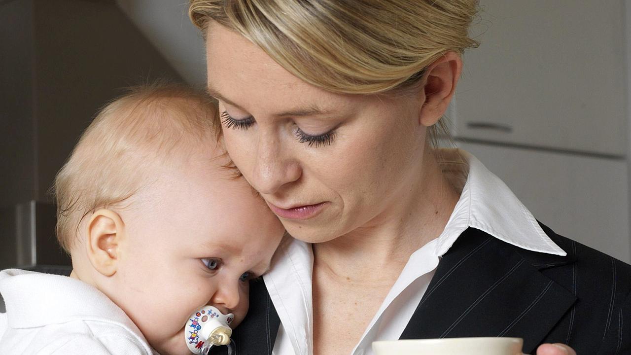 Eine Mutter im Business-Anzug mit ihrem Baby auf dem Arm, in der Hand eine Kaffeetasse.