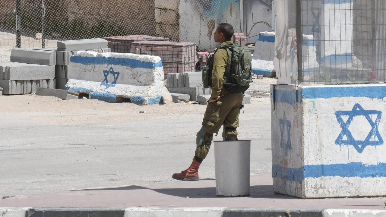 Israelische Kontrollstelle in Hebron im Westjordanland/Palaestina: Ein Israelischer Soldat in Uniform steht vor einem Wachhäuschen, das mit einer gemalten israelischen Flagge angestrichen ist.
