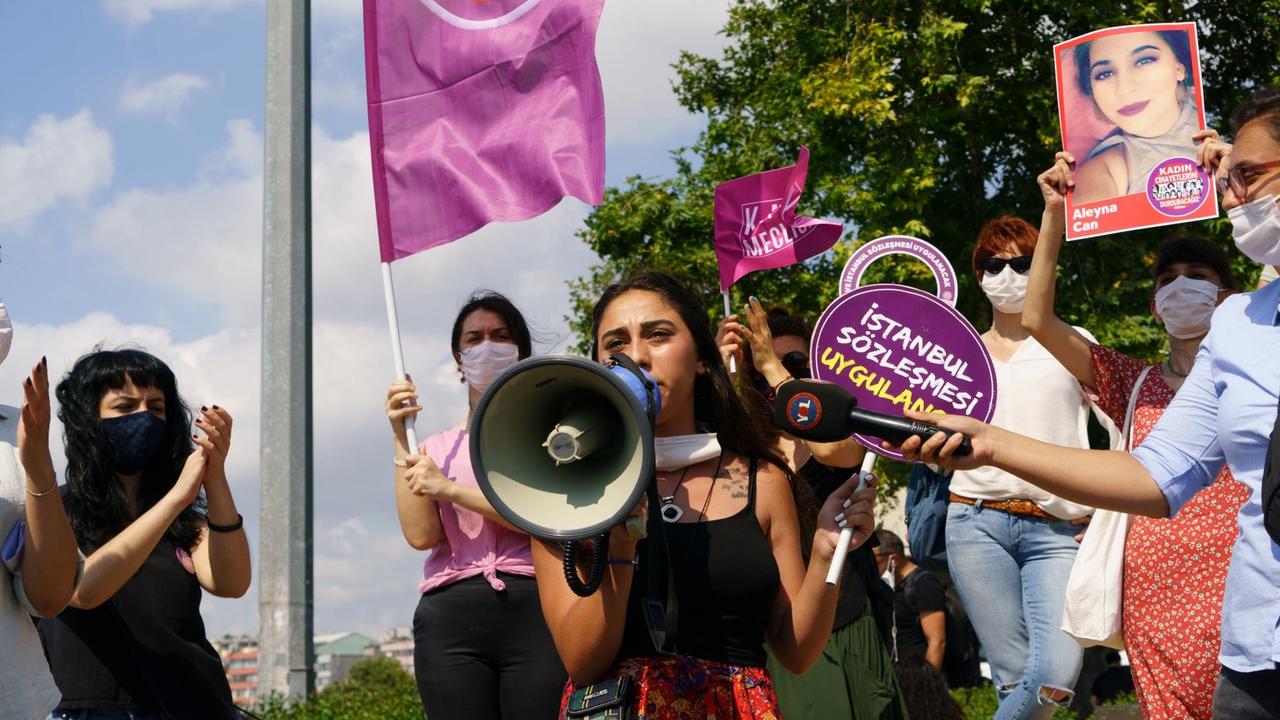 Eine junge Frau spricht während einer Demonstration inmitten andere klatschender Frauen in eine Megaphon.