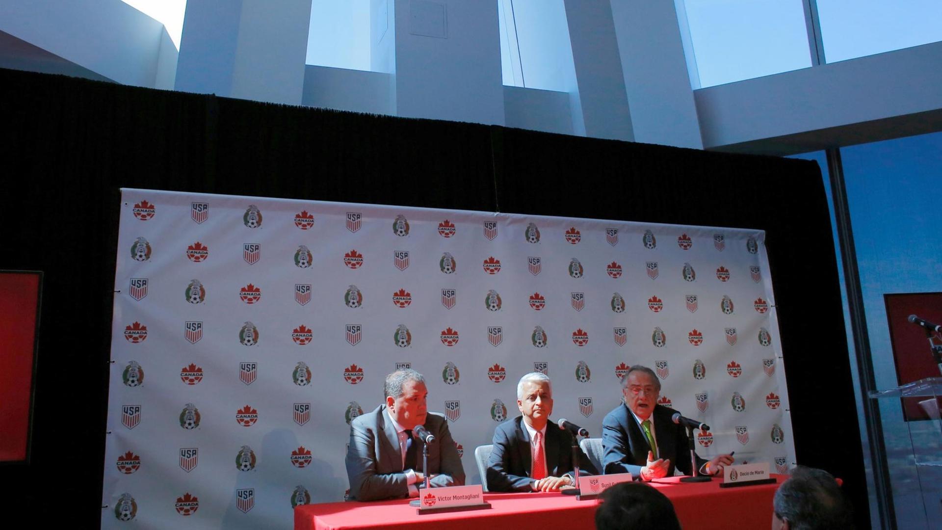 Die drei Fußballfunktionäre sitzen nebeneinander auf einem Podium. Die drei Fußballfunktionäre sitzen nebeneinander auf einem Podium.