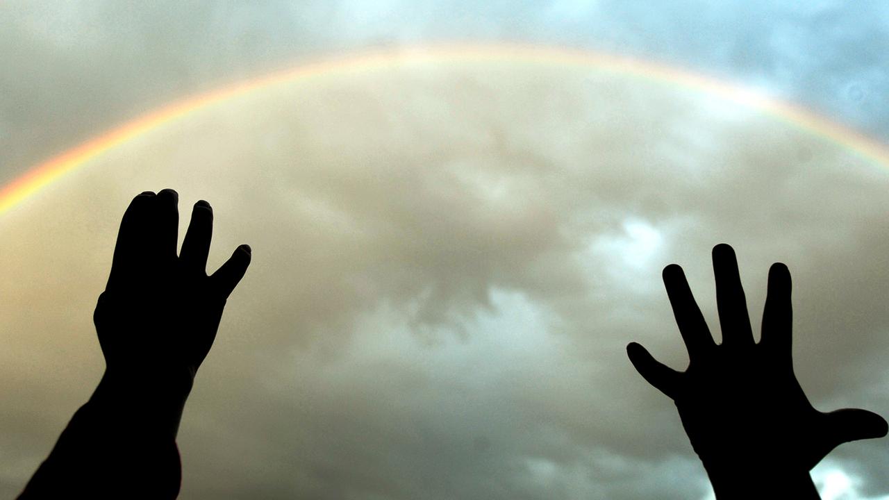 Ein Regenbogen, ausgestreckte Hände greifen danach