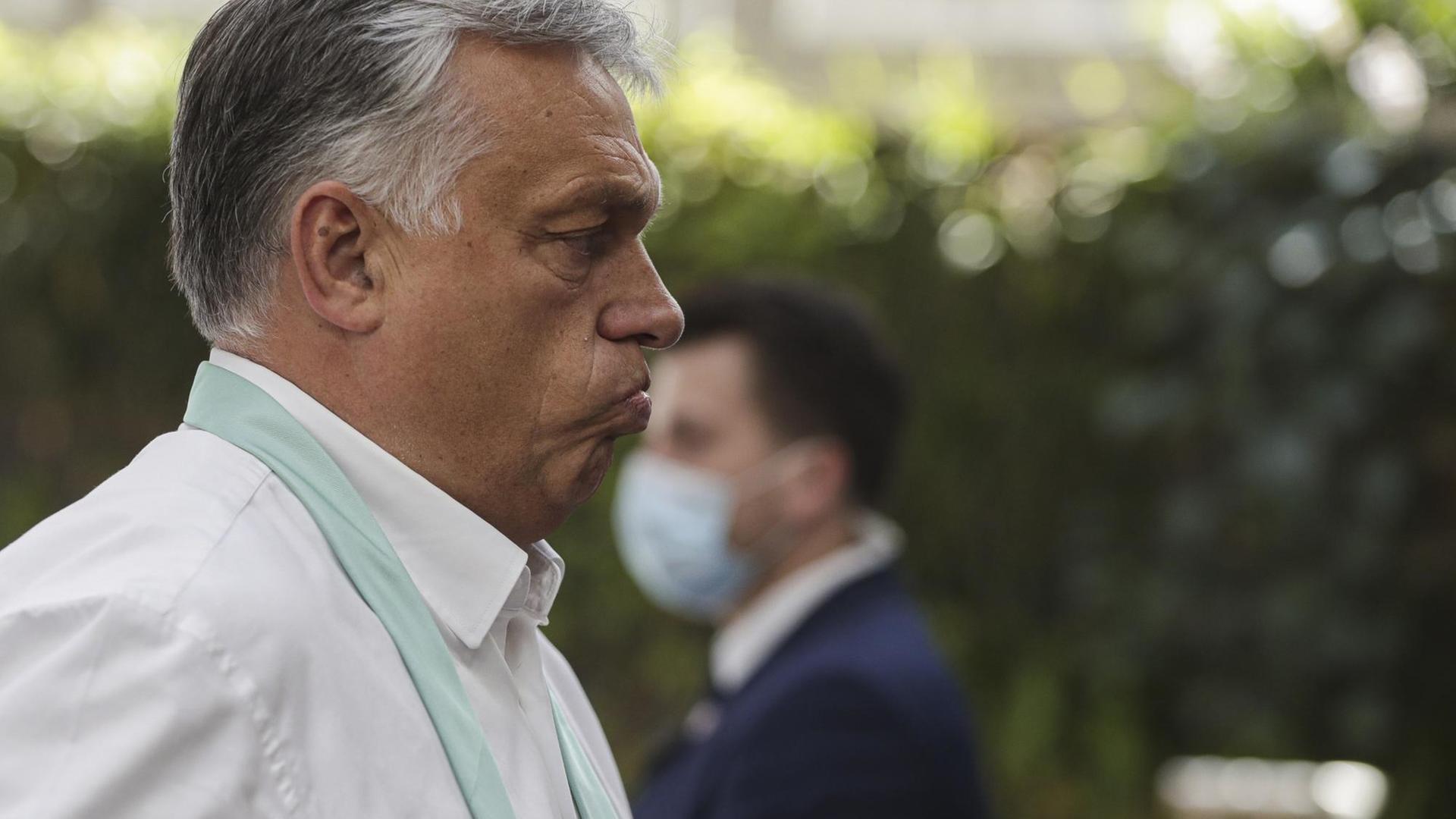 Zu sehen ist Viktor Orban, Premierminister von Ungarn. Im Hintergrund ein Mann mit Mund-Nasen-Bedeckung. Zu sehen ist Viktor Orban, Premierminister von Ungarn. Im Hintergrund ein Mann mit Mund-Nasen-Bedeckung.