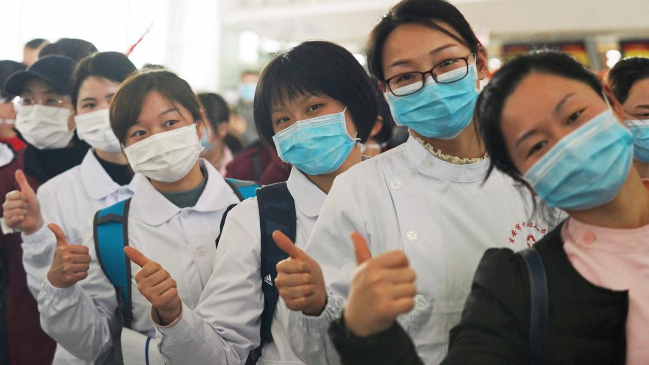 Mitglieder eines chinesischen medizinischen Versorgungsteams stellen sich in einer Reihe auf, um ein Flugzeug zu besteigen. Sie strecken den Daumen nach oben und signalisieren, dass alles ok ist.