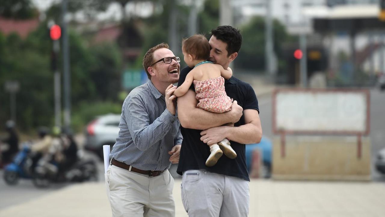 Ein Mann trägt ein kleines Mädchen auf dem Arm, ein zweiter Mann daneben lacht das Kind an.