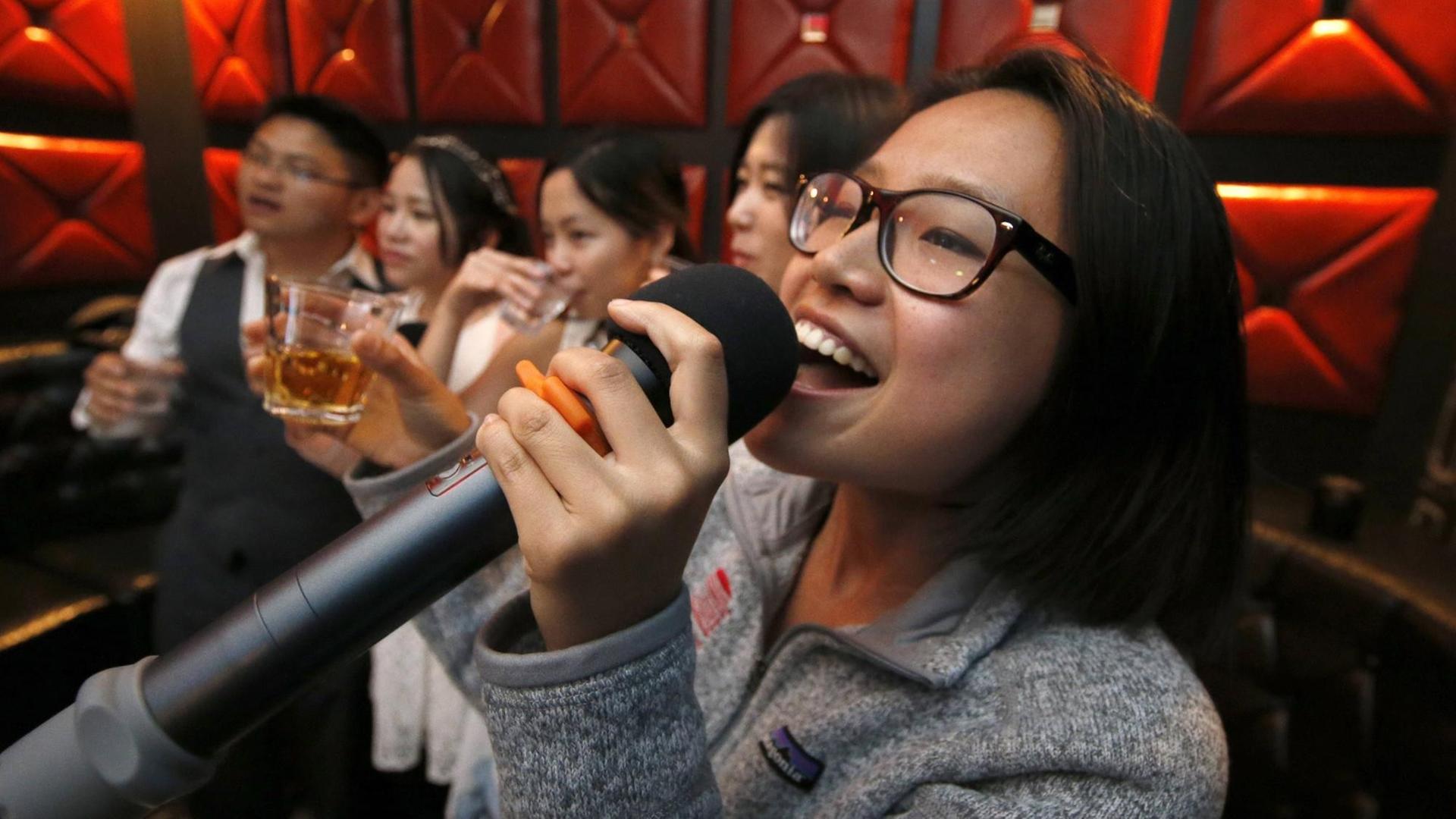 Eine Frau singt mit weiteren Gästen in einer Karaoke-Bar Eine Frau singt mit weiteren Gästen in einer Karaoke-Bar