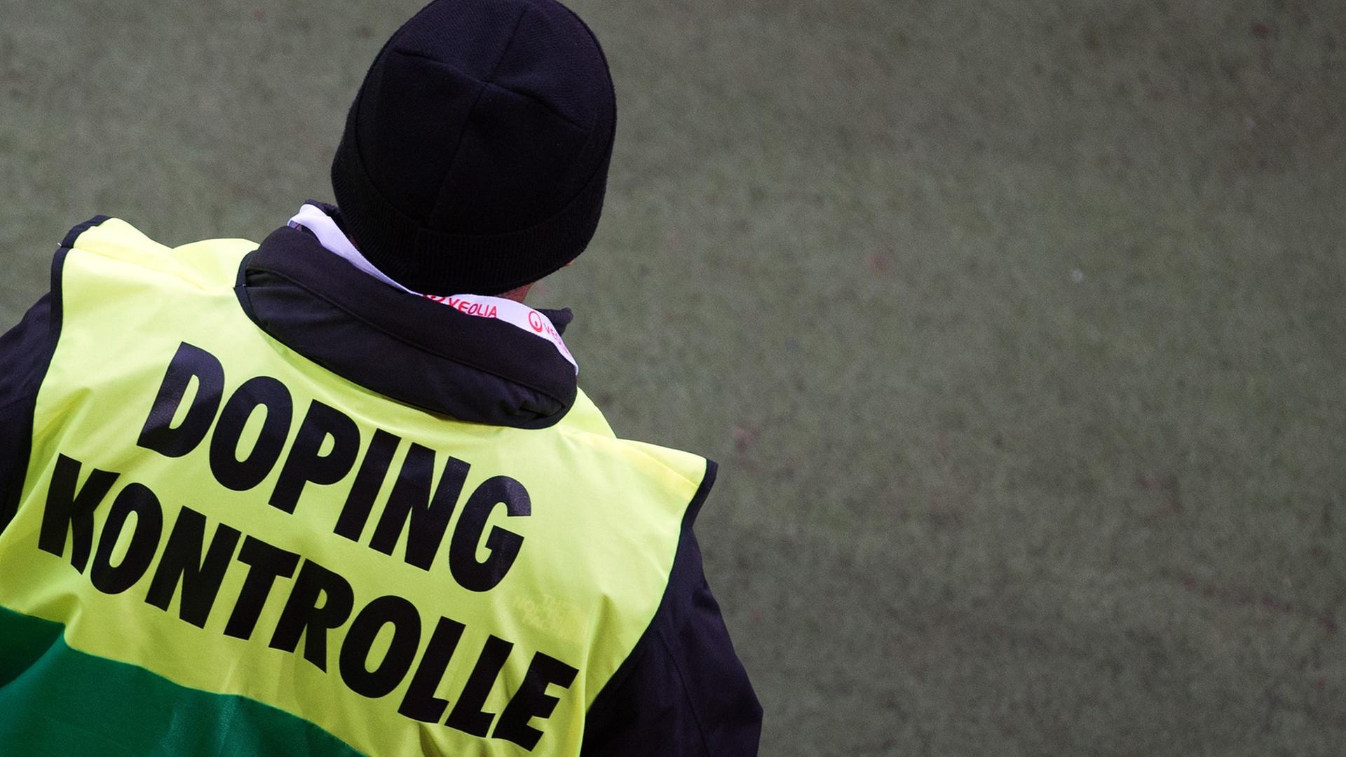 Ein Dopingkontrolleur von hinten mit gelb-grüner Jacke und der Aufschrift "Dopingkontrolle".
