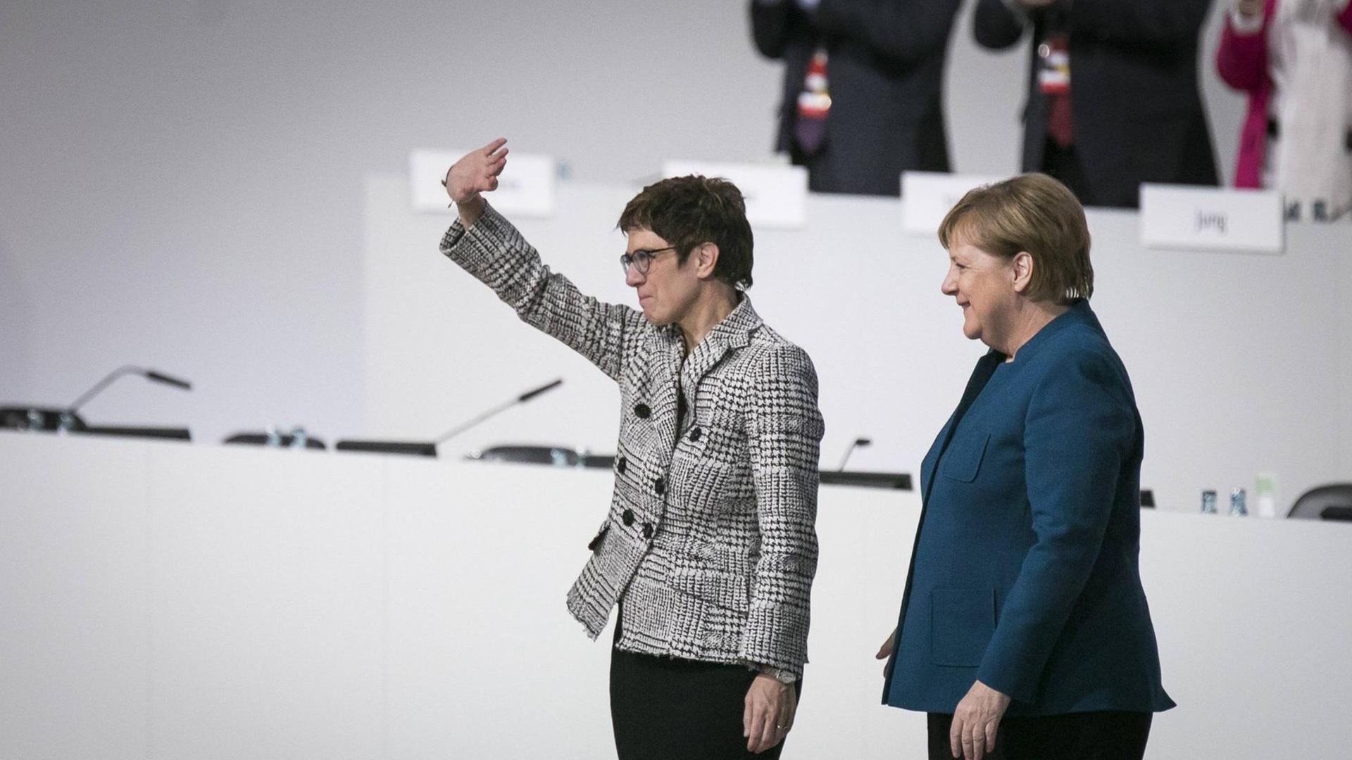 Annegret Kramp-Karrenbauer winkt ins Publikum, rechts neben ihr steht Angela Merkel in lockerer Pose Annegret Kramp-Karrenbauer winkt ins Publikum, rechts neben ihr steht Angela Merkel in lockerer Pose