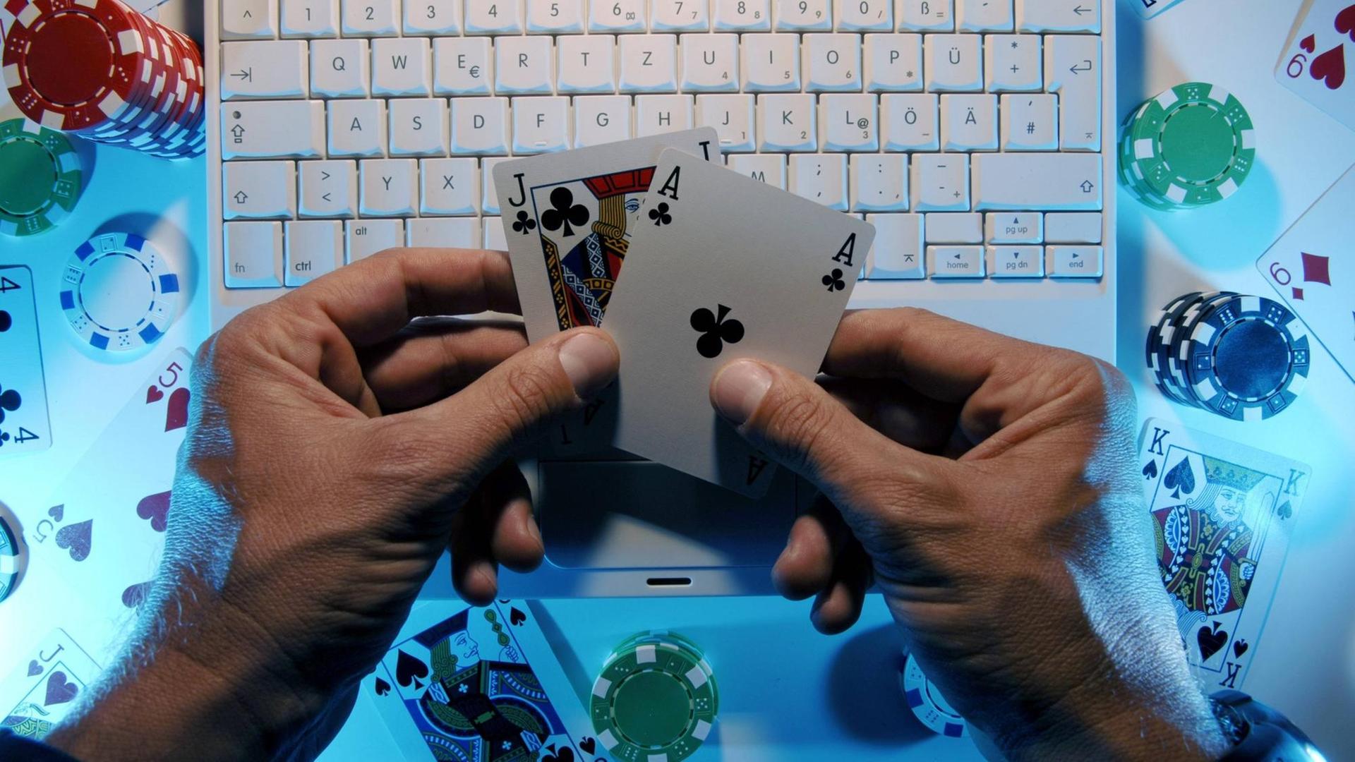 Hände eines Onlinepokerspielers halten ein Buben und ein Ass vor einer Computertastatur. Hände eines Onlinepokerspielers halten ein Buben und ein Ass vor einer Computertastatur.