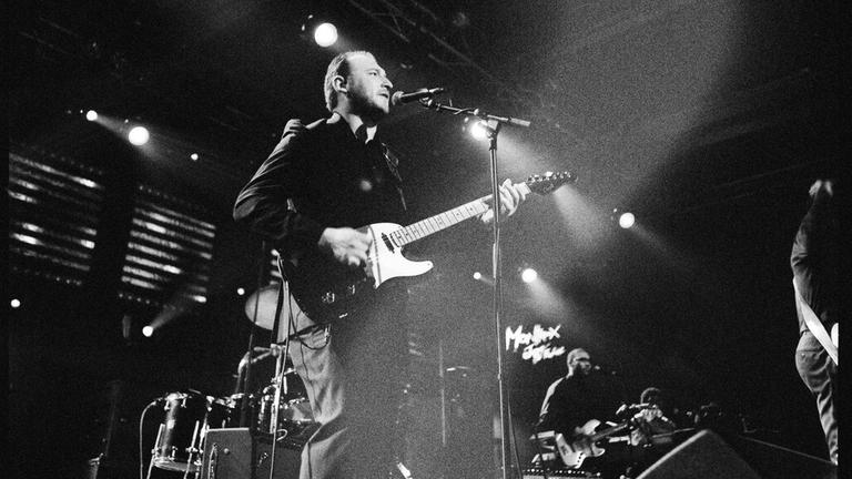 Schwarz-weiß-Bild einer Band, die auf einer Konzertbühne steht.
