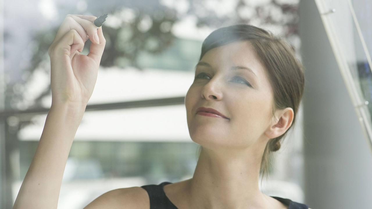 Eine Frau steht in einem Büro und hält einen Stift in der Hand, um etwas zu schreiben. Eine Frau steht in einem Büro und hält einen Stift in der Hand, um etwas zu schreiben.