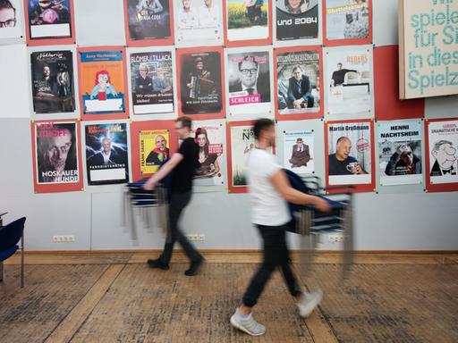 Mitarbeiter tragen Stühle durch die Kleinkunstbühne Unterhaus in Mainz. Im Hintergrund ist eine Wand mit Plakaten zu sehen.