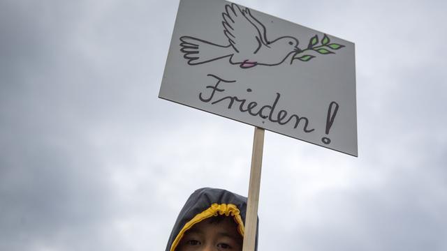 Ein Kind trägt am Potsdamer Platz in Berlin ein Plakat mit einer Friedenstaube