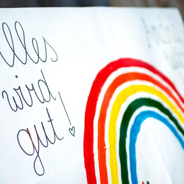 Ein Schild mit der Aufschrift "Alles wird gut!" und einem gemalten Regenbogen haengt im Fenster eines geschlossenen Eiscafes.