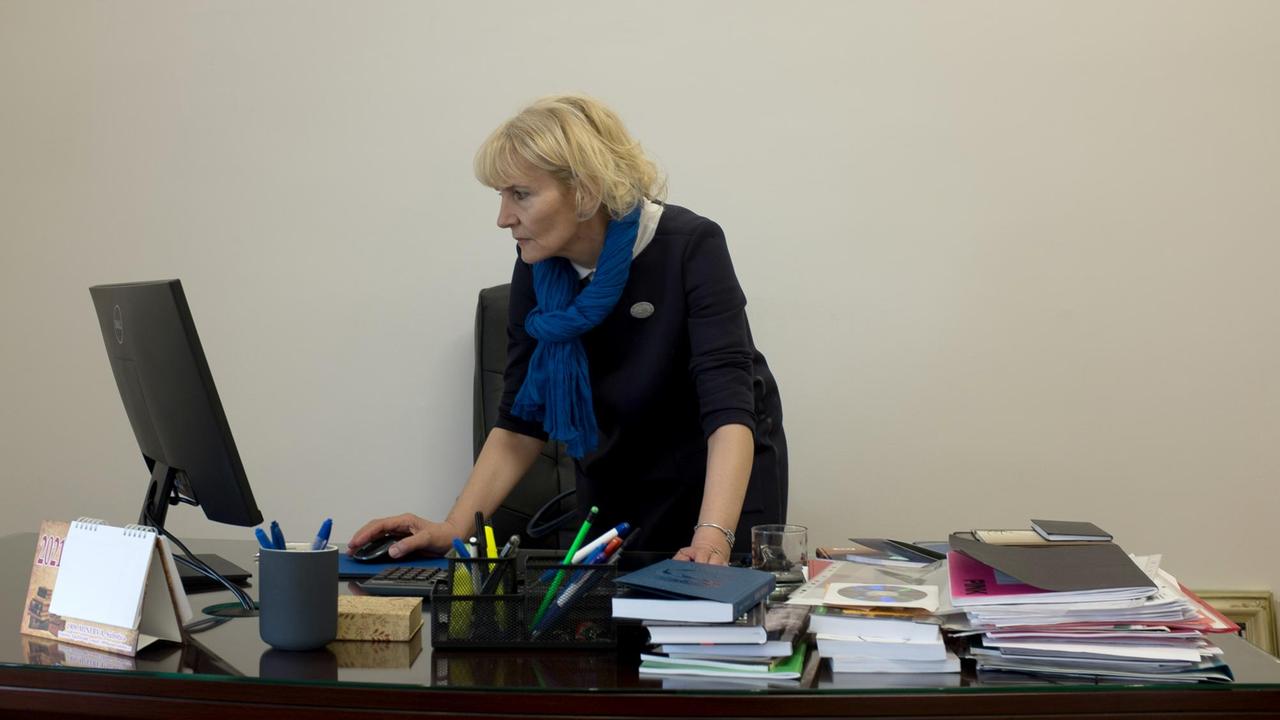 Bora Babic steht an ihrem Schreibtisch auf dem viele Bücher und Papier legen und ein Computerbildschirm steht Bora Babic steht an ihrem Schreibtisch auf dem viele Bücher und Papier legen und ein Computerbildschirm steht