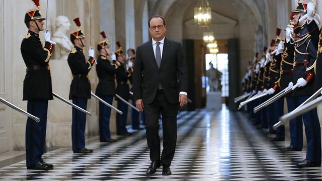 Hollande läuft einen Gang entlang. Rechts und links salutieren Mitglieder einer Garde mit Schwertern.