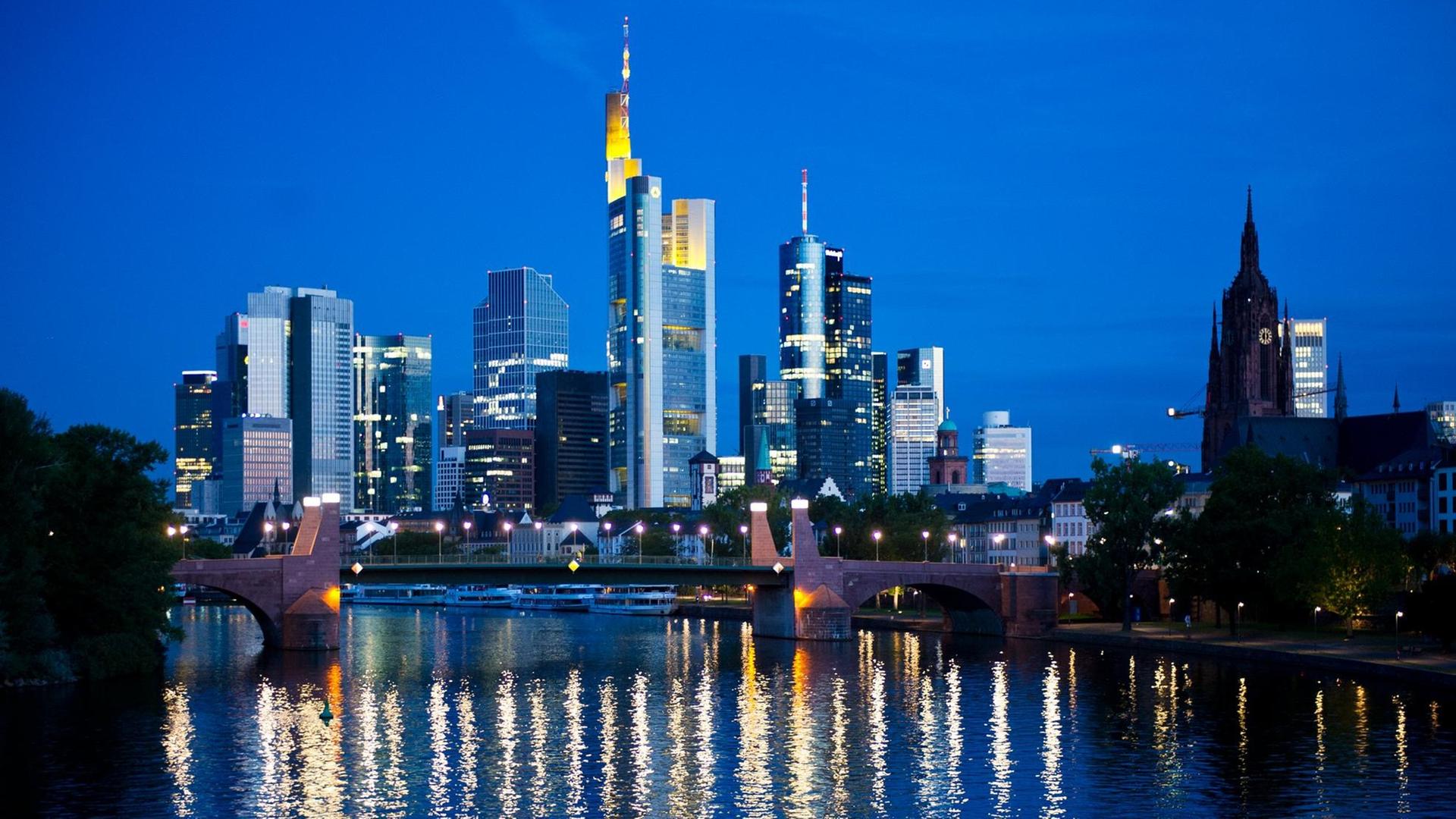 Im ersten Licht des Tages spiegeln sich am 26.08.2015 die Lichter der Skyline von Frankfurt am Main (Hessen) zur morgentlichen blauen Stunde im Fluss.