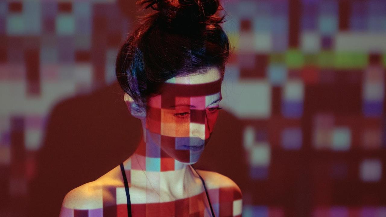 Eine junge Frau steht in einer Lichtprojektion, die aus farbigen Quadraten besteht.