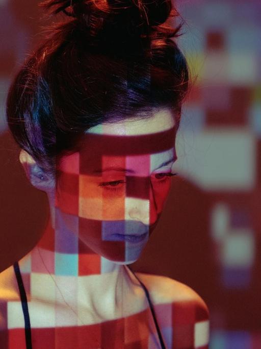 Eine junge Frau steht in einer Lichtprojektion, die aus farbigen Quadraten besteht.