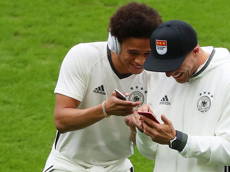 Leroy Sane (l.) und Lukas Podolski zeigen sich etwas auf dem Smartphone.