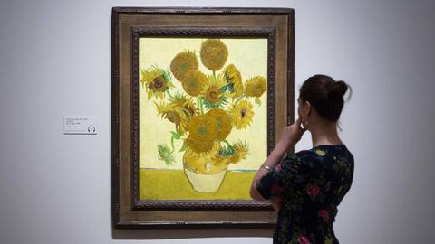 Eine Frau steht rechts von dem "Sonnenblumenbild" von Van Gogh und betrachtet es.