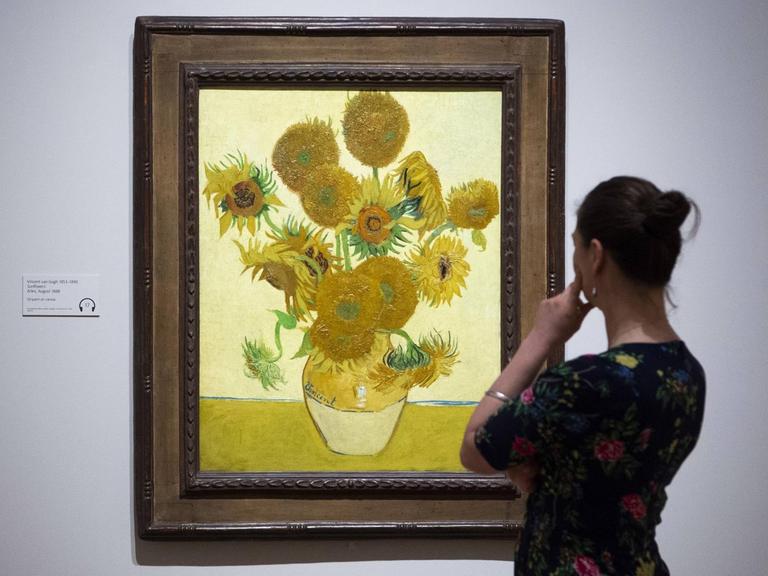 Eine Frau steht rechts von dem "Sonnenblumenbild" von Van Gogh und betrachtet es.