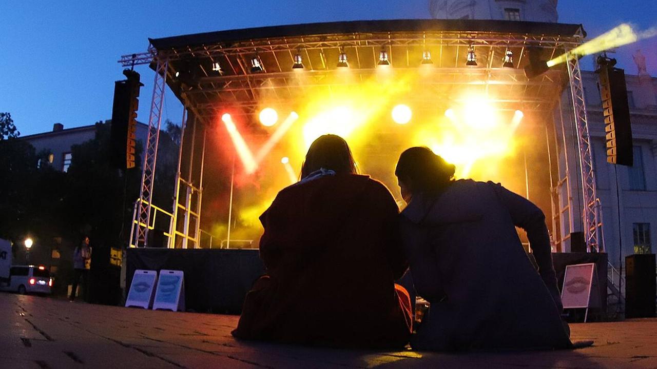 Zwei Menschen sitzen auf dem Boden vor der Open-Air Bühne bei den Musikfestspielen Potsdam Sanssouci. Zwei Menschen sitzen auf dem Boden vor der Open-Air Bühne bei den Musikfestspielen Potsdam Sanssouci.