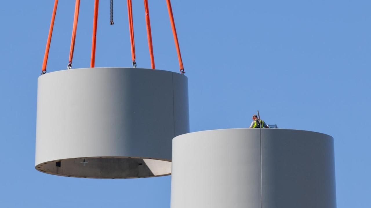 Ein weiteres Stahlsegment wird mit Hilfe eines Krans auf den Turm einer neuen Windenergieanlage gesetzt. Ein weiteres Stahlsegment wird mit Hilfe eines Krans auf den Turm einer neuen Windenergieanlage gesetzt.