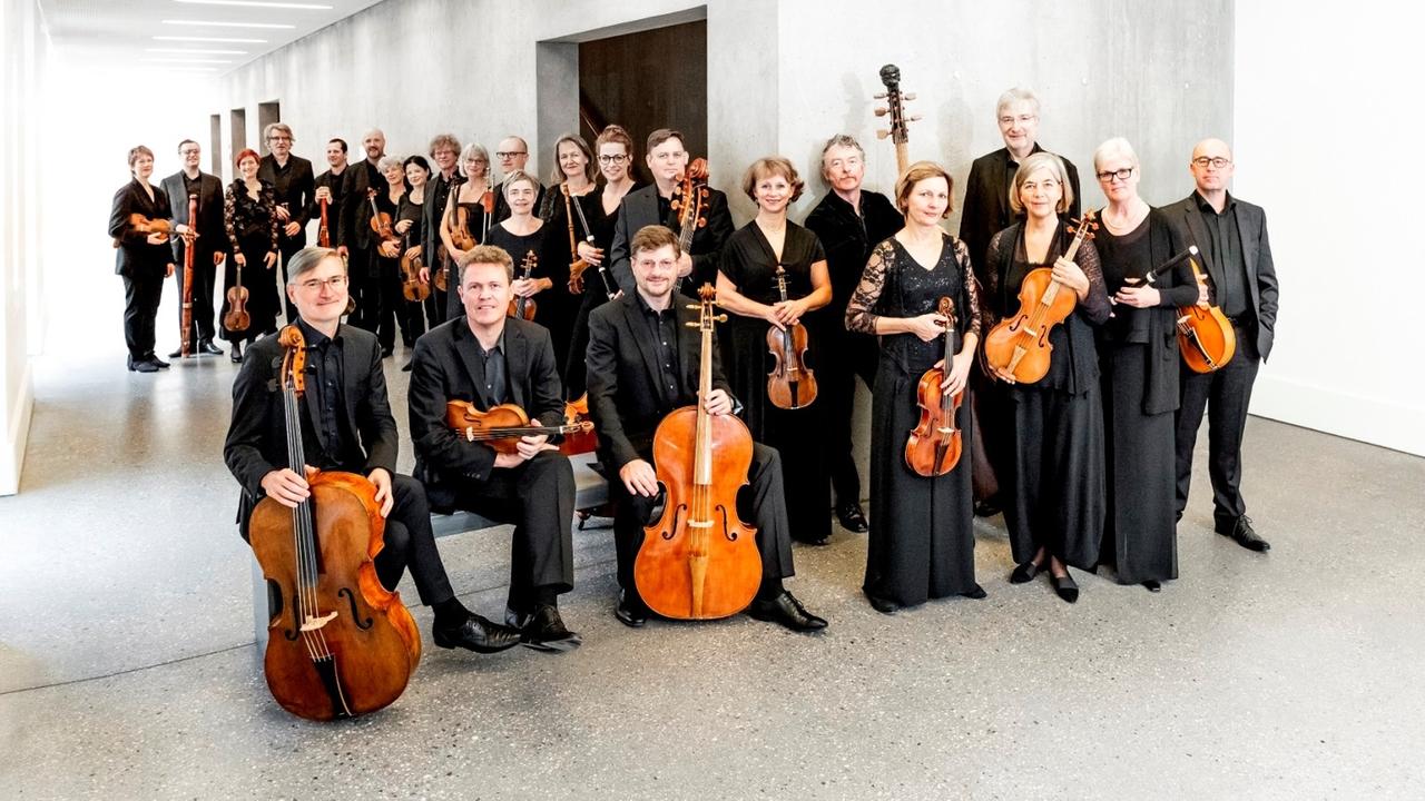 Viele Menschen mit Orchesterinstrumenten in der Hand stehen in einem weißen Raum. Viele Menschen mit Orchesterinstrumenten in der Hand stehen in einem weißen Raum.
