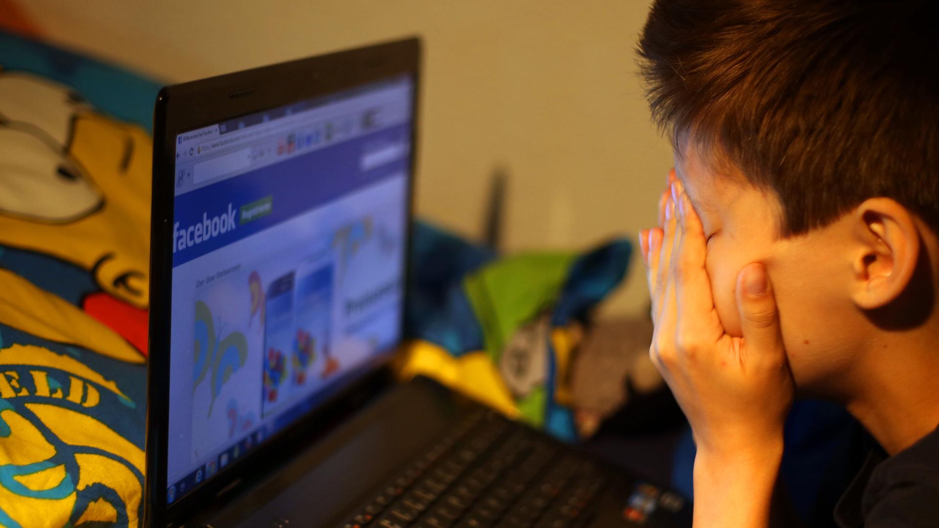 Ein Junge reibt sich vor seinem Laptop beim betrachten der Facebook-Seite die Augen.