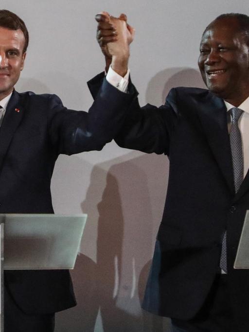 Die Präsidenten Frankreichs und der Elfenbeinküste, Macron und Ouattara, heben gemeinsam ihre Arme in die Höhe.