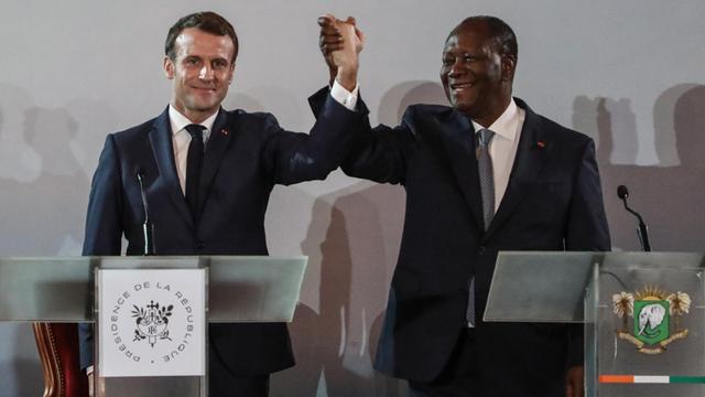 Die Präsidenten Frankreichs und der Elfenbeinküste, Macron und Ouattara, heben gemeinsam ihre Arme in die Höhe.