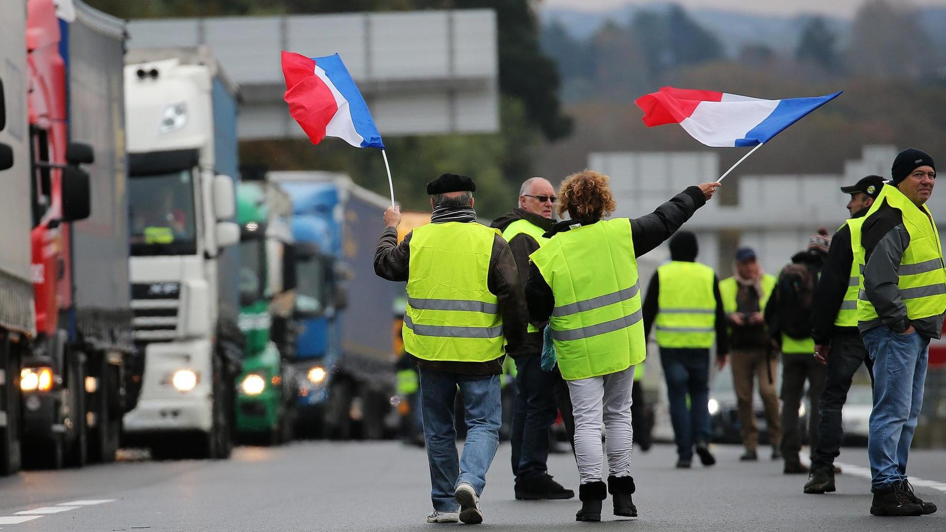 Demonstranten schwenken französische Flaggen, während sie Lastwagen auf der Autobahn blockieren.