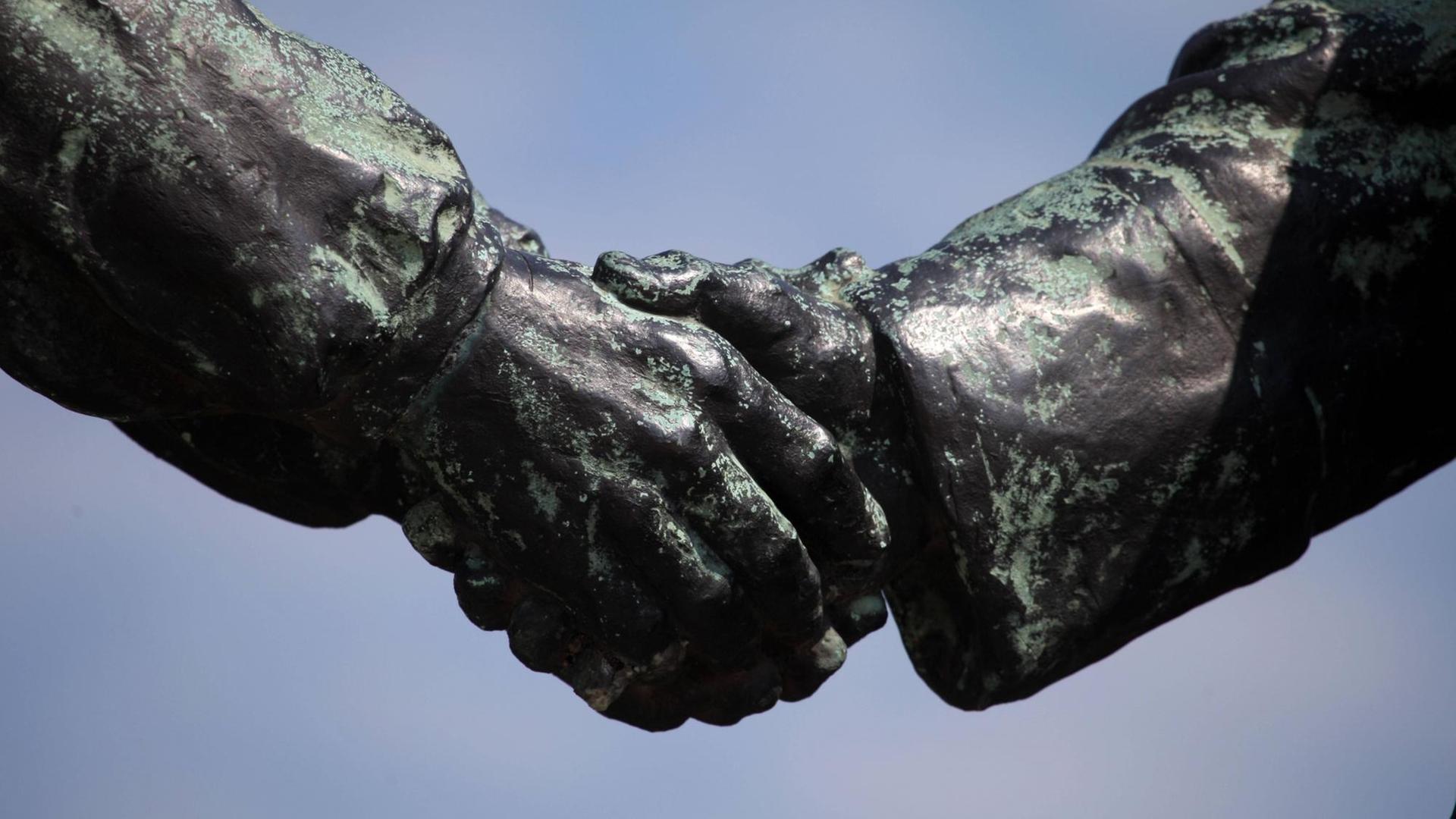 Zwei Hände von Bronzefiguren reichen einander die Hände. Zwei Hände von Bronzefiguren reichen einander die Hände.