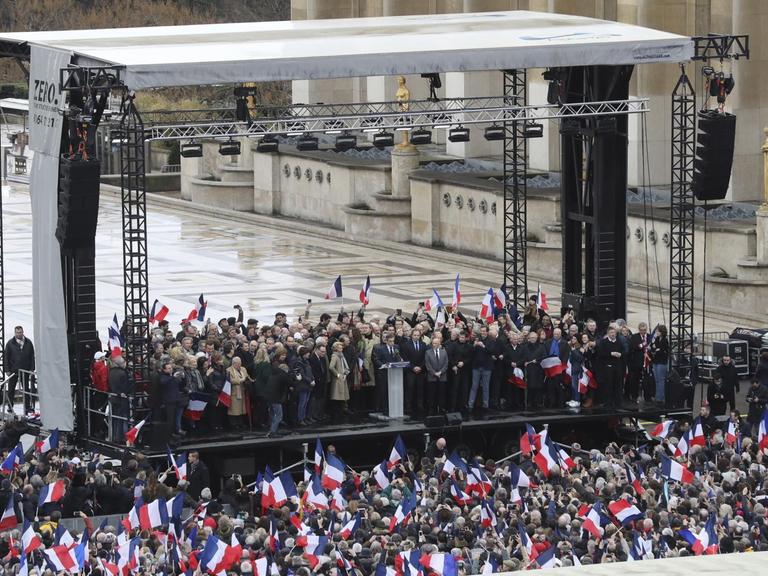 Sie sehen eine Tribüne und davor eine Menschenmenge auf dem Trocadero-Platz in Paris. Der Politiker François Fillon hält eine Rede.