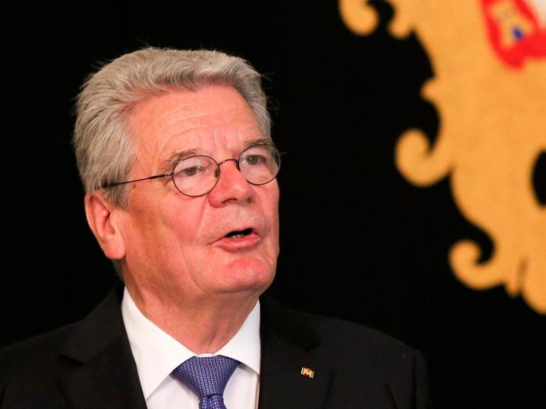 Joachim Gauck hält vor einem Wappen vor schwarzem Hintergrund eine Rede