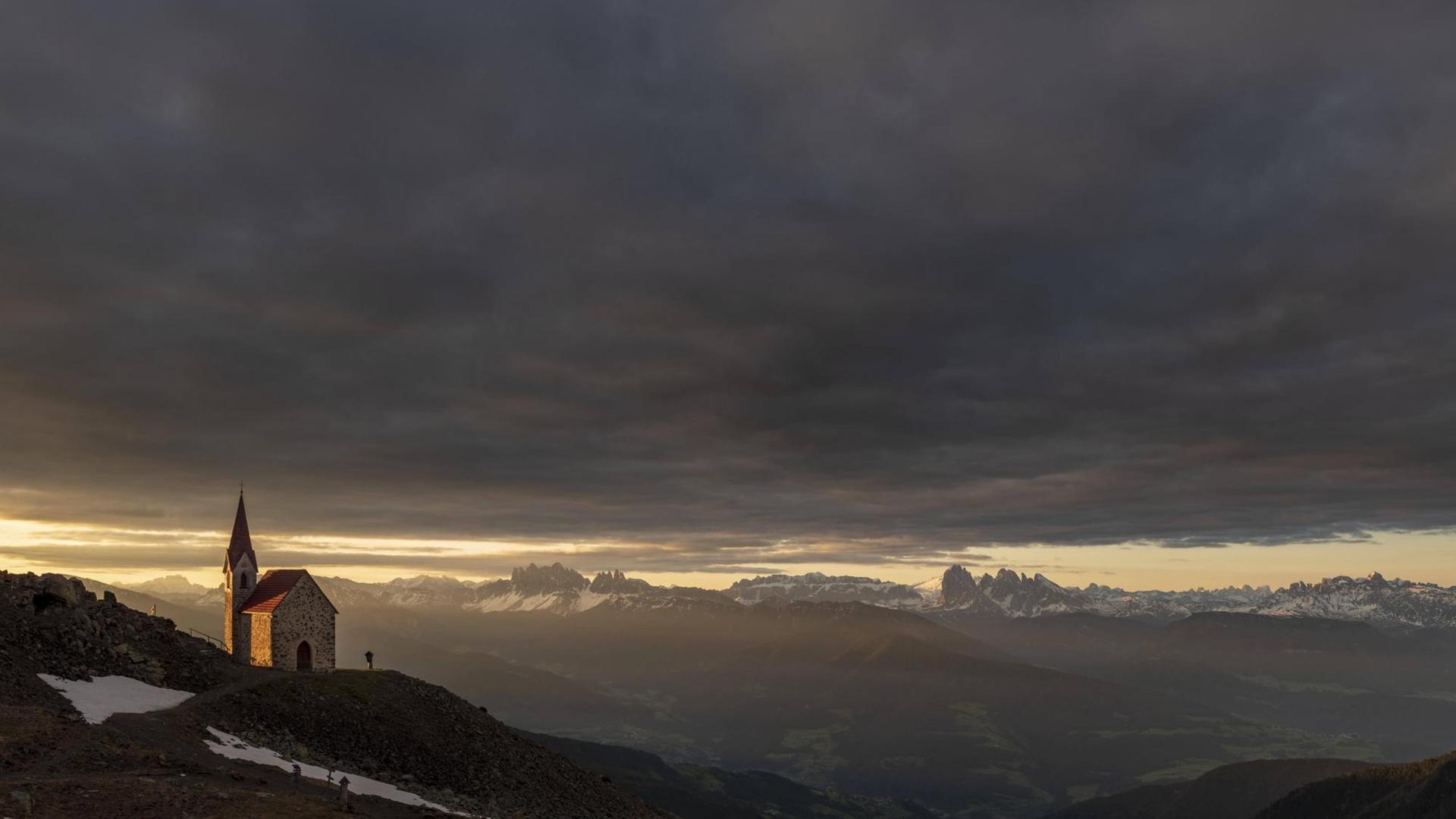 Eine Kirche in den Bergen steht vor dramatischen Himmel vor einer gewaltigen Gebirgskulisse. Eine Kirche in den Bergen steht vor dramatischen Himmel vor einer gewaltigen Gebirgskulisse.